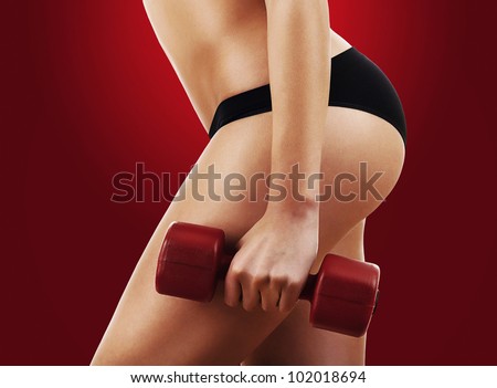 sporty woman hips and red dumbbell on red background