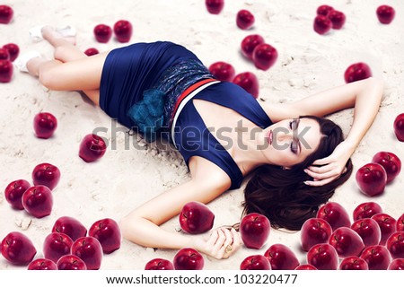 woman with red apples on the sand in blue dress