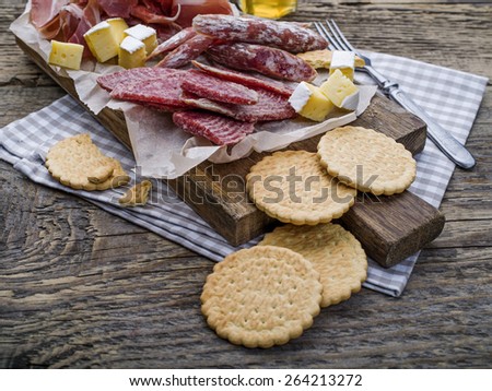 Chopping board with meat selection and cheese on dark wooden background