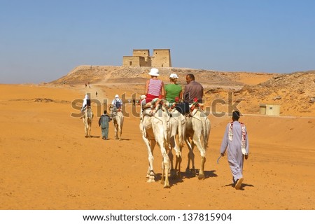 LAKE NASSER, EGYPT-NOV 28:Tourists ride camel in desert toward ruined temple of Dakka. The ancient Egypt Ptolemaic temple dedicate to Thoth of the Sycamore Fig. Nov 28, 2007. Lake Nasser, Egypt.