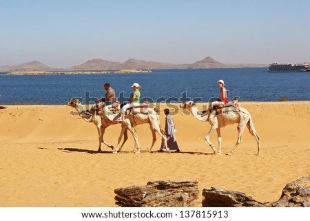 LAKE NASSER, EGYPT-NOV 28:Tourists ride camel in desert toward ruined temple of Dakka. The ancient Egypt Ptolemaic temple dedicate to Thoth of the Sycamore Fig. Nov 28, 2007. Lake Nasser, Egypt.