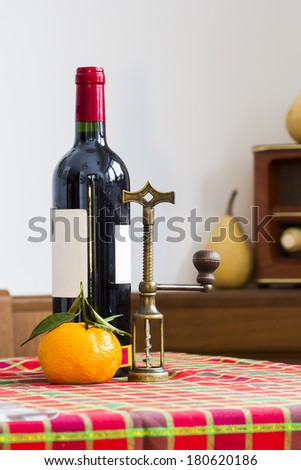 Still life composition with copper corkscrew, bottle of wine and mandarin on colored table cloth