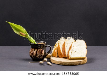Still life composition with wooden kitchen cutting board, bread and ceramic pot with Arum flower on dark background