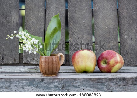 Red apples and lily of the valley flower in a ceramic small mug with old wood background