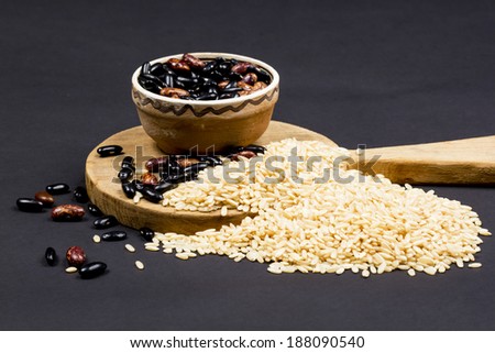 Composition with beans in a ceramic pot, paddy rice and wooden kitchen cutting board on dark background