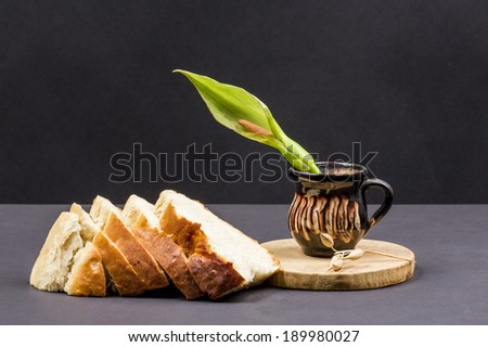Still life composition with wooden kitchen cutting board, bread and ceramic pot with Arum flower on dark background