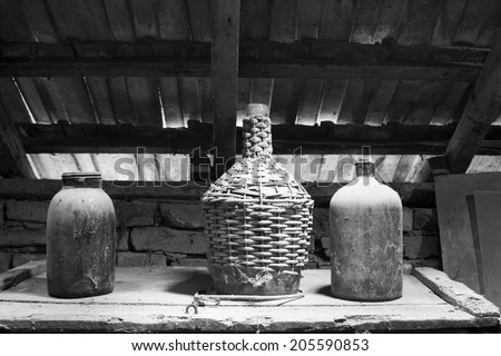 Black and white photo of glass, wooden and metallic objects in the attic with dust and spiderwebs in a beautiful, moody light