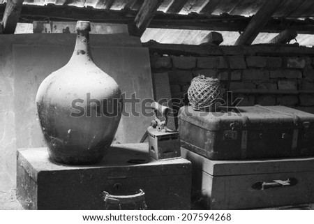Black and white photo of glass, wooden and metallic objects in the attic with dust and spiderwebs in a beautiful, moody light