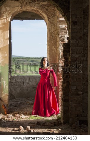 Beautiful, brunette woman in an old, abandoned house, waring a red dress, looking sad and melancholic