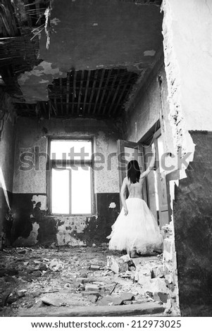 Sad mood in an old, abandoned house with girl half dressed at the natural light from the window. Photo has grain texture visible on its maximum size. Artistic black and white photography