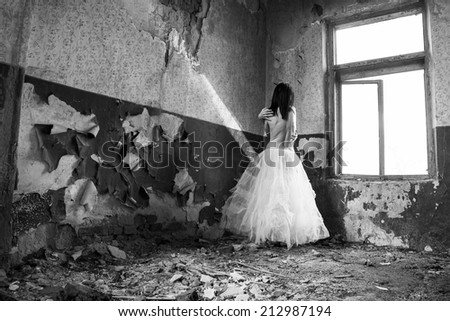 Sad mood in an old, abandoned house with girl half dressed at the natural light from the window.  Photo has grain texture visible on its maximum size.  Artistic black and white photography