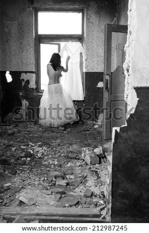 Sad mood in an old, abandoned house with girl half dressed at the natural light from the window.  Photo has grain texture visible on its maximum size.  Artistic black and white photography