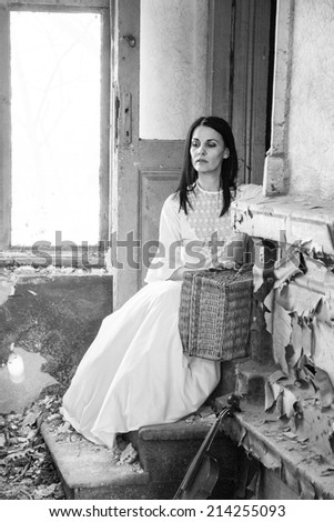 Sad mood in an old, abandoned house with girl wearing an old fashioned wedding dress with natural light.   Photo has grain texture visible on its maximum size.  Artistic black and white photography