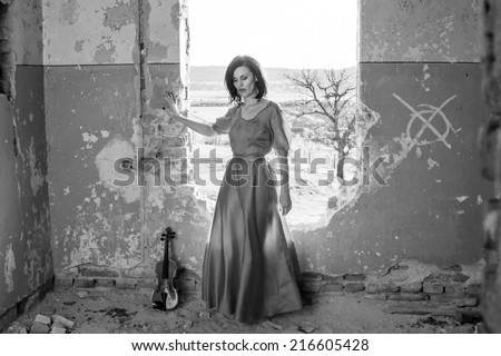 Beautiful, brunette woman in an old, abandoned house, wearing an orange  dress, looking sad and melancholic. Photo has grain texture visible on its maximum size. Artistic black and white photography