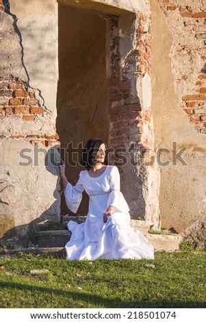 Beautiful, brunette woman in an old, abandoned house, wearing a wedding dress, posing with sunset light. Photo has grain texture visible on its maximum size. Artistic  photography