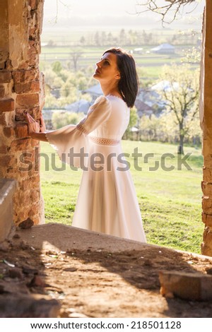 Beautiful, brunette woman in an old, abandoned house, wearing a wedding dress, posing with sunset light. Photo has grain texture visible on its maximum size. Artistic  photography