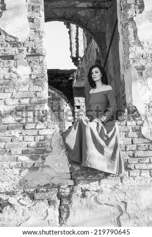 Beautiful, brunette woman in an old, abandoned house, wearing an orange dress, looking sad and melancholic. Photo has grain texture visible on its maximum size. Artistic black and white photography