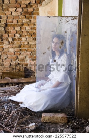 Beautiful girl shot through a dirty glass in an abandoned house wearing an old fashioned wedding dress. Photo has grain texture visible on its maximum size. Artistic photography