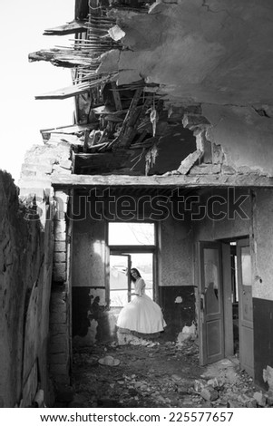 Sad mood in an old, abandoned house with girl wearing an old fashioned wedding dress with natural light. Photo has grain texture visible on its maximum size. Artistic, black and white photography