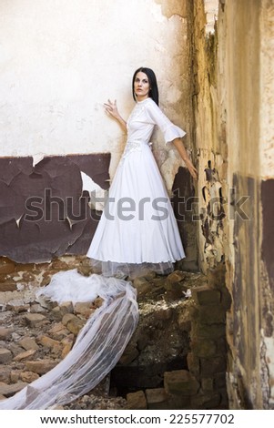 Sad mood in an old, abandoned house with girl wearing an old fashioned wedding dress with natural light. Photo has grain texture visible on its maximum size. Artistic photography