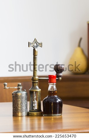 Still life composition with metallic pepper grinder, small bottle of aromatic vinegar and copper corkscrew on wooden table
