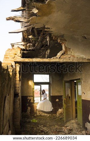 Sad mood in an old, abandoned house with girl wearing an old fashioned wedding dress with natural light. Photo has grain texture visible on its maximum size. Artistic photography