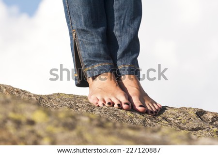 Woman legs, feet and hands with jeans, on a rock, with natural background and fluffy, white clouds