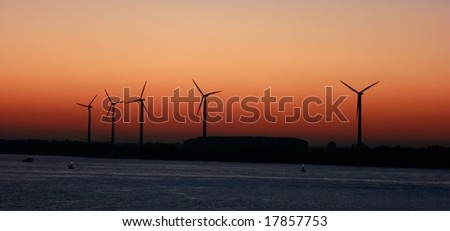 Silhouettes of wind turbines by dusk