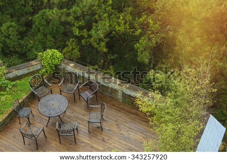 Wooden deck surrounded by trees with seating arrangement with steel metal framed table and chairs by look down.