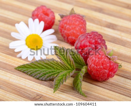Fresh Ripe Raspberries with Leaf and White Chamomile Flower on Old Wooden Hardboard
