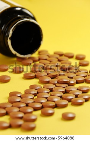 a spilled bottle of pills against yellow background. Shallow DOF.