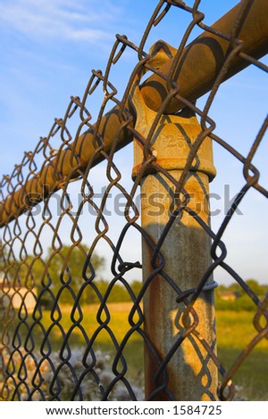 Rusty fence post and chain link fence with blue sky background