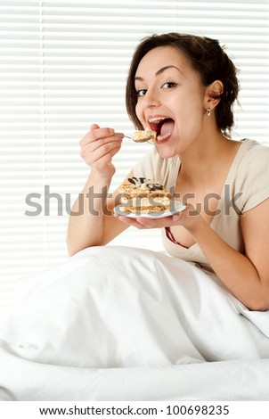 Young Caucasian female sitting in bed with a cake on a light background