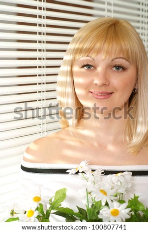 Portrait of a luck blonde Caucasian lady with flowers on a light background