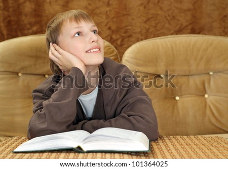 Beautiful Caucasian boy sitting on the couch with a book on a brown background