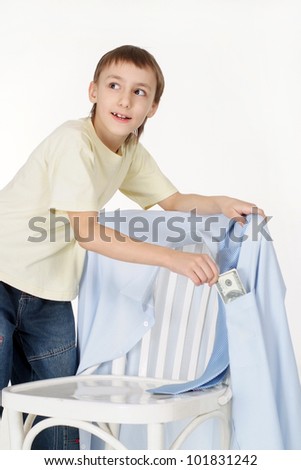 Handsome young boy gets money from the shirts hanging on a chair on a white background