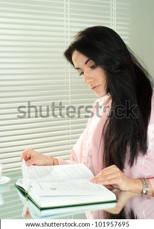 Beautiful Brunette Caucasian sitting with a book on a light background