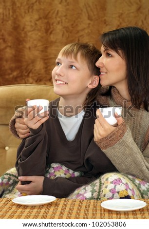 Beautiful mom and son sitting on the couch with a cup on a brown background