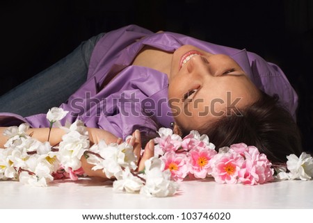 Tanned girl in the purple shirt lies among flowers and lovingly looks