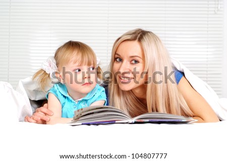 Beautiful caucasian mom and daughter lying on the bed with a book