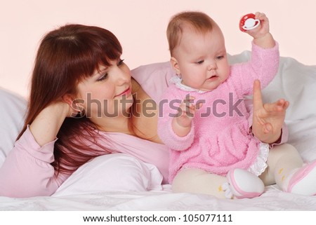 A beautiful Caucasian mama with her daughter lying in bed on a light background