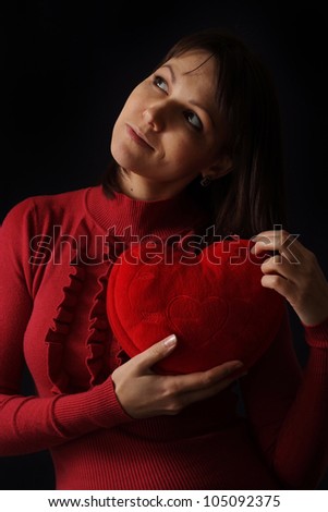 Pretty Caucasian woman with a happy heart pillow on a dark background