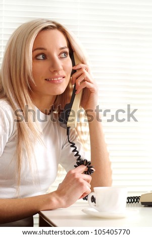 Pretty Caucasian woman sitting with a phone on a light background