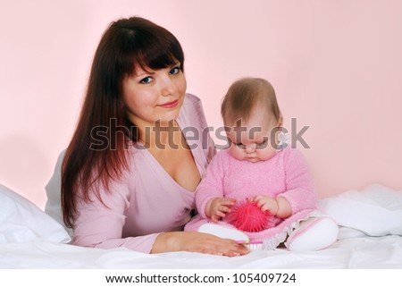 A beautiful Caucasian mother with her daughter lying in bed on a light background
