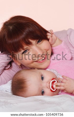 A nice Caucasian mummy with her daughter lying in bed on a light background
