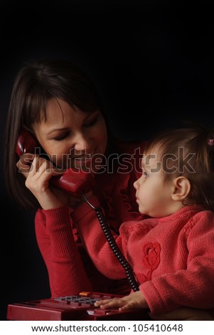 Happy Caucasian happy mother and daughter talk on the phone on a dark background