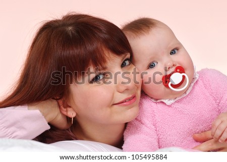 A beautiful Caucasian mom with her daughter lying in bed on a light background