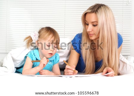 Pretty caucasian mother and daughter lying on the bed with a pencils
