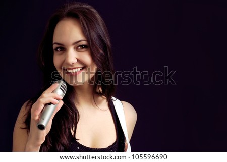 Pretty Caucasian young woman posing with a microphone on a dark background