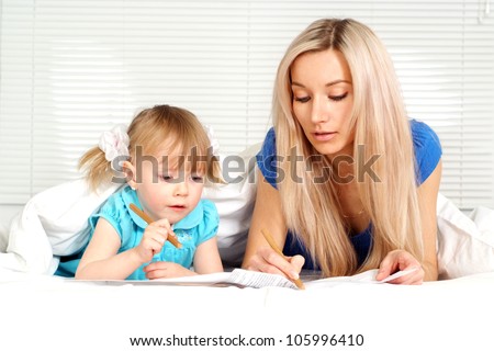 Beautiful mother and daughter lying on the bed with a pencils